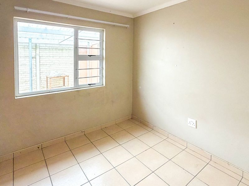 A vacant bedroom featuring tiled flooring, a built-in cupboard, and a window with security bars, offering a clean canvas for personalization.