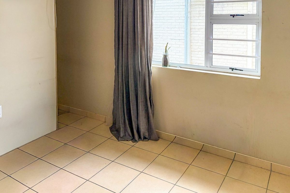 A vacant bedroom featuring tiled flooring, an aluminium window with security bars, and neutral wall finishes, ready for personal touches.