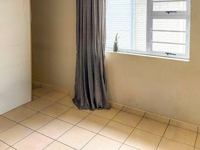 A vacant bedroom featuring tiled flooring, an aluminium window with security bars, and neutral wall finishes, ready for personal touches.