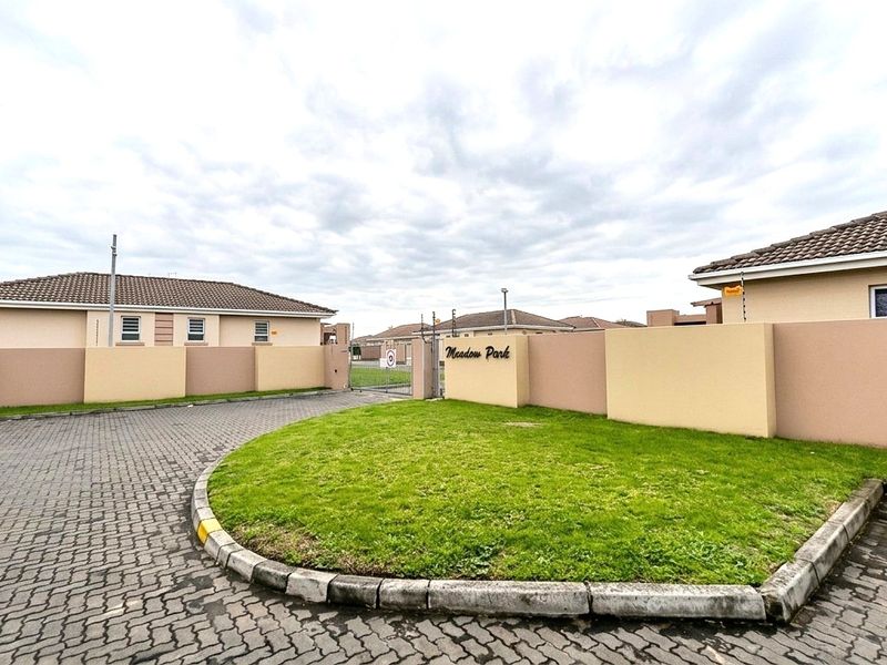 Entrance view of Meadow Park residential estate featuring paved driveway, perimeter walling with electric fencing, and well-maintained landscaped grounds.