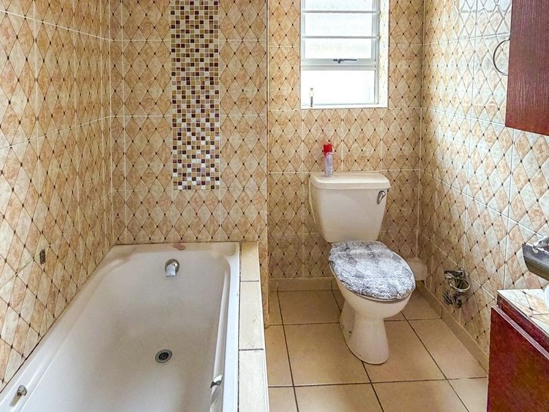 A functional bathroom featuring a built-in bathtub, toilet, and vanity cabinet with a washbasin, finished with decorative ceramic wall and floor tiles.