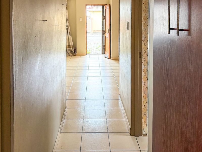 A vacant hallway featuring neutral ceramic floor tiles, leading towards an exterior doorway with access to the rear of the property.