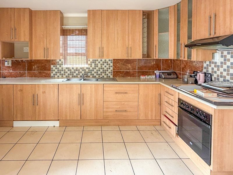 A functional kitchen featuring wood-look laminate cabinetry, a double basin sink, built-in oven, extractor fan, and tiled splashback with ceramic floor tiles.