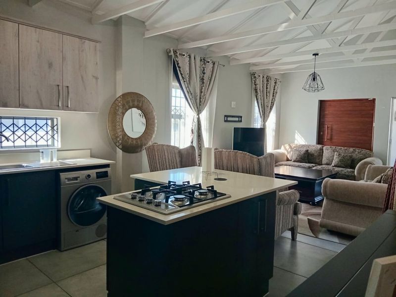 Open-plan living area featuring a modern kitchen island with gas hob, exposed beam ceilings, and tiled flooring, seamlessly connecting to the lounge space.