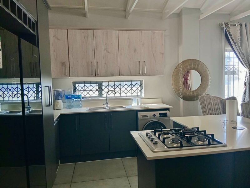 Modern kitchen featuring dark lower cabinetry, light wood-look upper cabinets, stone countertops, a gas hob, and an integrated washing machine.