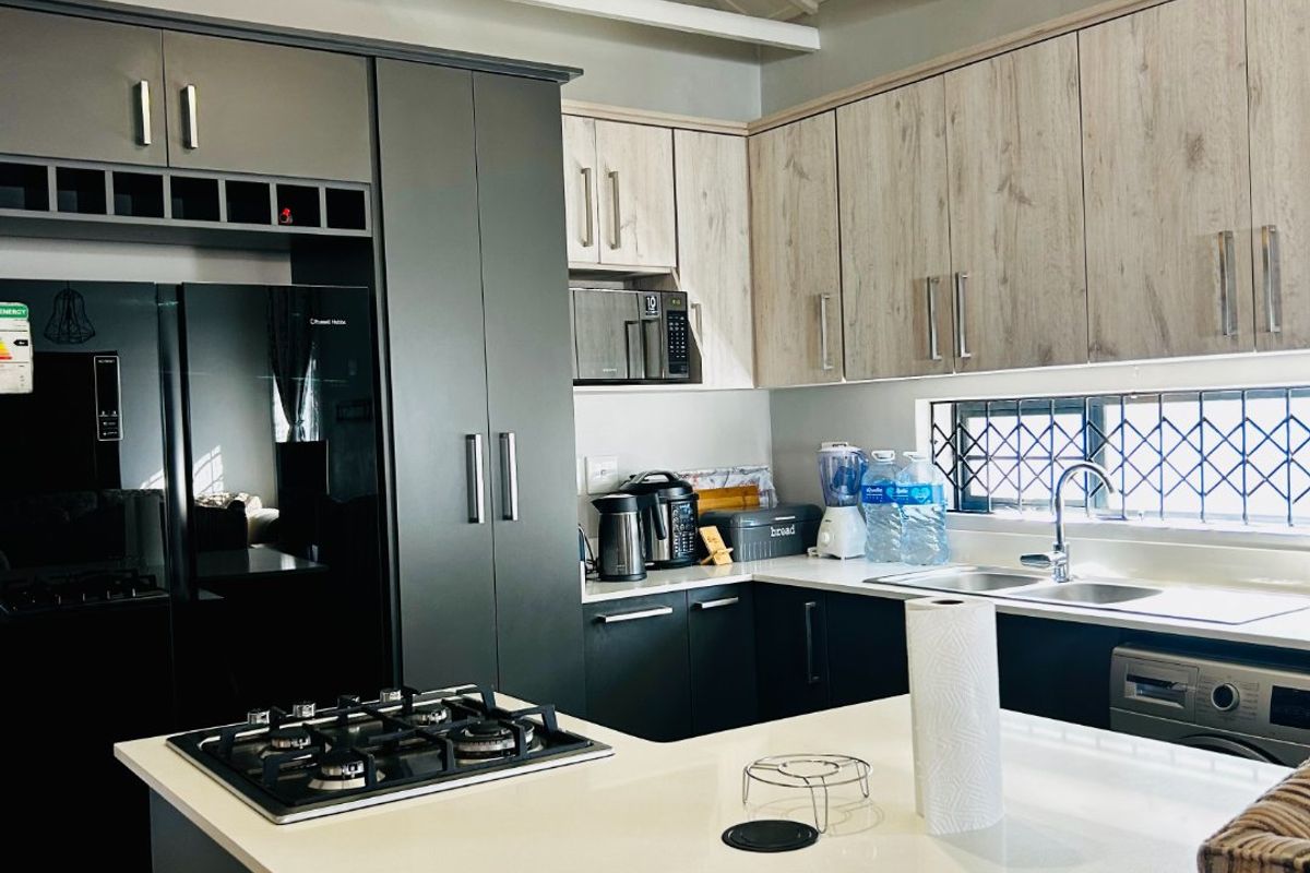 Modern kitchen featuring two-tone cabinetry, quartz countertops, a central island with a gas hob, and exposed white roof trusses.