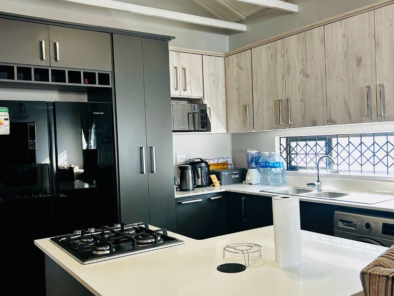 Modern kitchen featuring two-tone cabinetry, quartz countertops, a central island with a gas hob, and exposed white roof trusses.