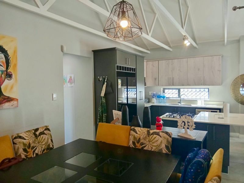 Open-plan kitchen and dining area featuring exposed white roof trusses, modern dark cabinetry, stone countertops, and a gas hob.
