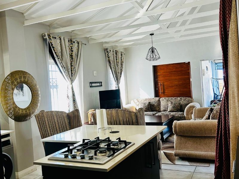 Open-plan living area featuring a kitchen island with a gas hob, exposed white timber ceiling beams, and neutral tiled flooring throughout.
