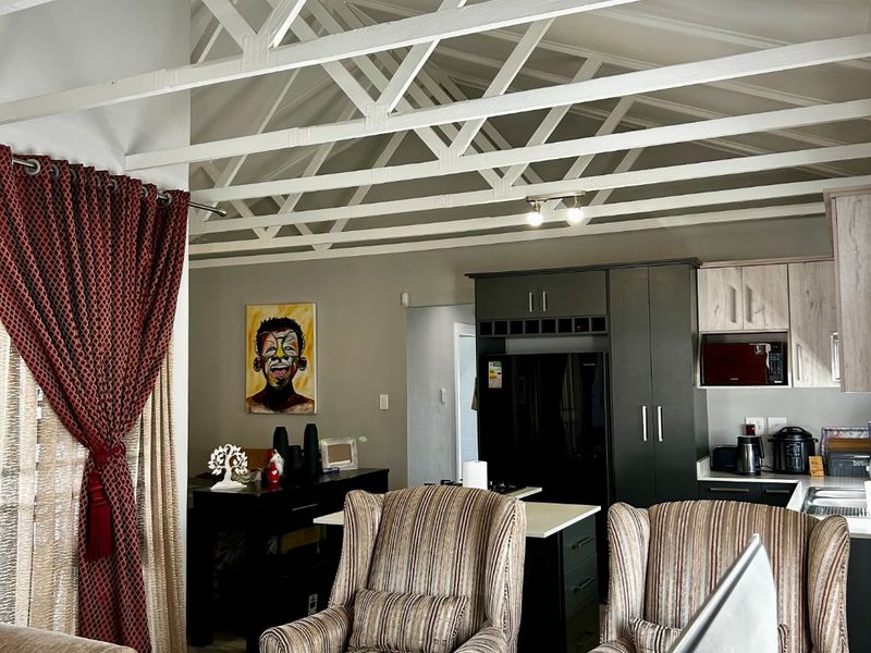 Open-plan living and kitchen area featuring high ceilings with exposed white trusses, modern cabinetry, and a central kitchen island.