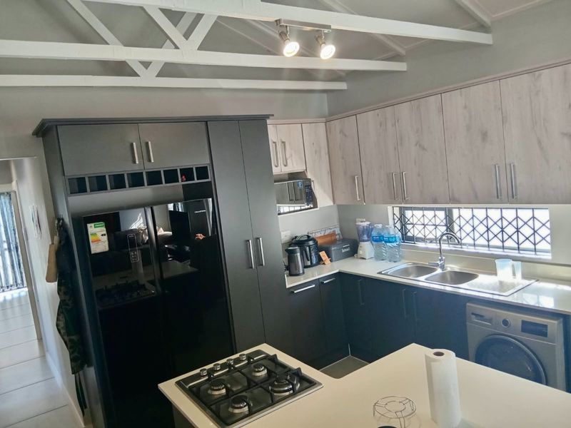 Modern kitchen featuring two-tone cabinetry, gas hob, double sink, and exposed white roof trusses, offering a functional and contemporary cooking space.
