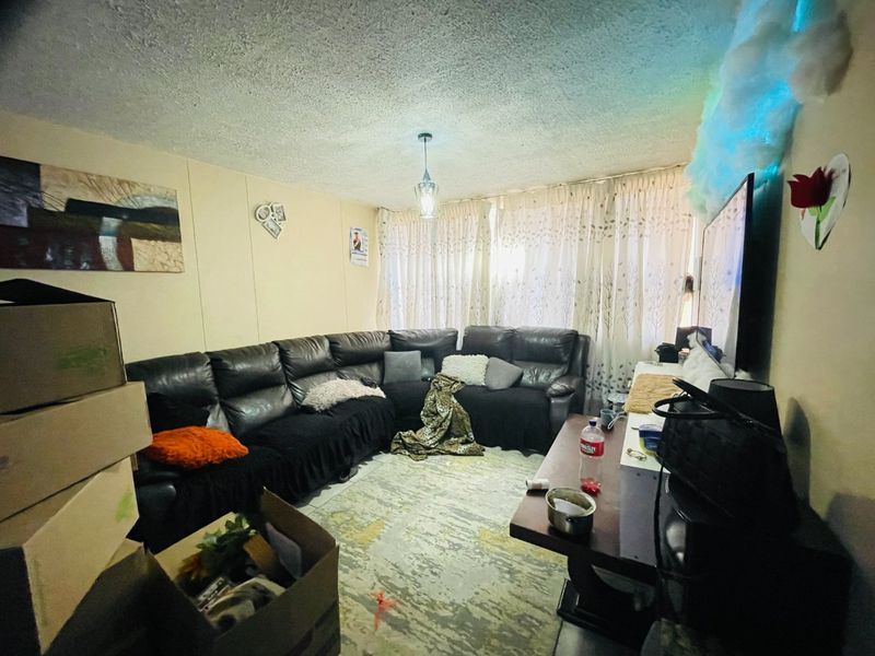 A living room space featuring a textured ceiling and window curtain tracks, currently used as a lounge area.