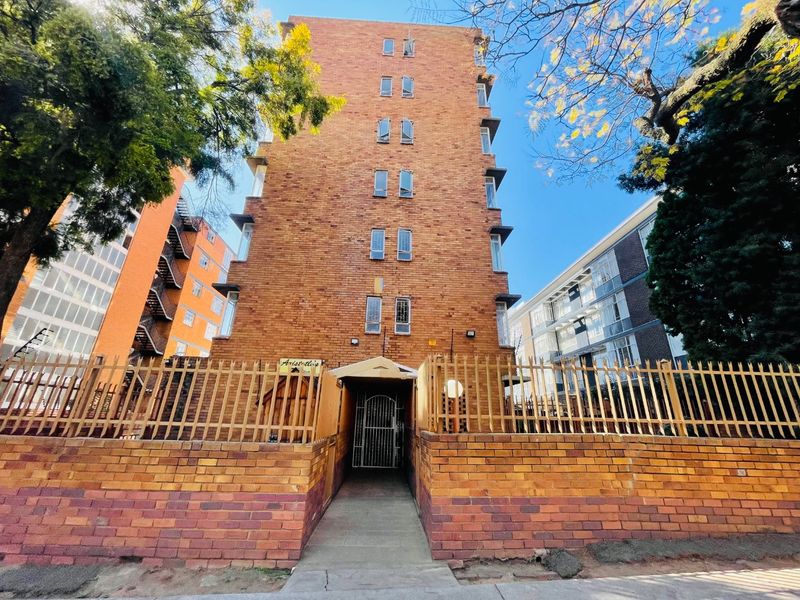Front elevation of a multi-story brick apartment building featuring secure perimeter fencing and a gated pedestrian entrance.