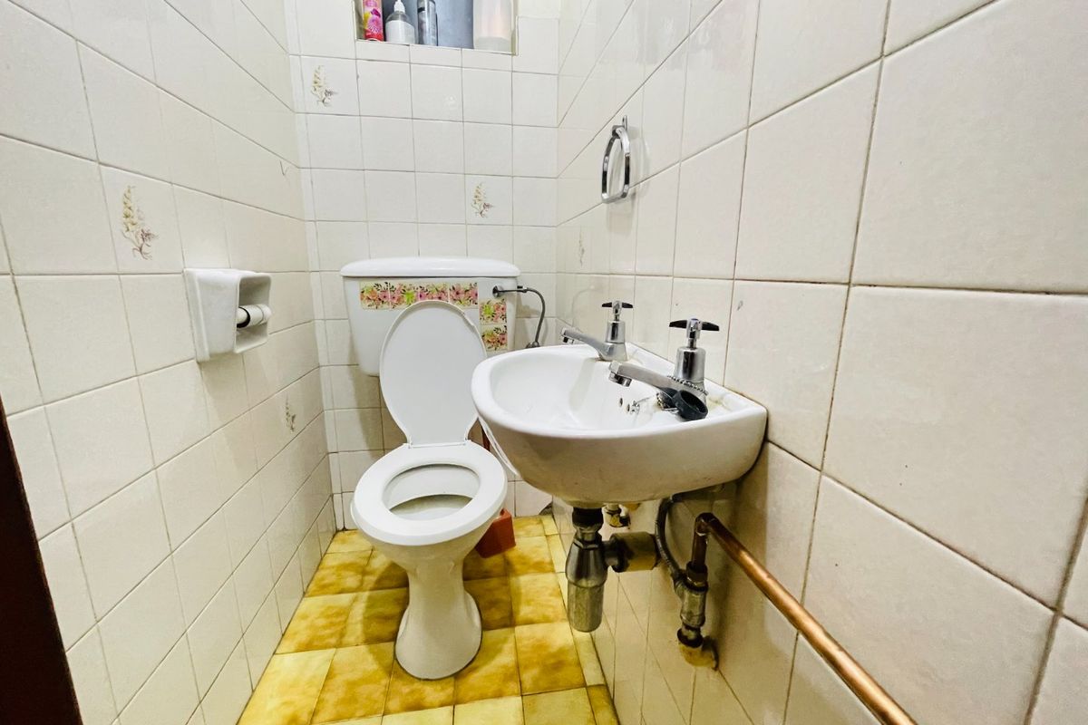 A compact bathroom featuring dated wall and floor tiles, a pedestal washbasin with exposed plumbing, and a standard toilet.