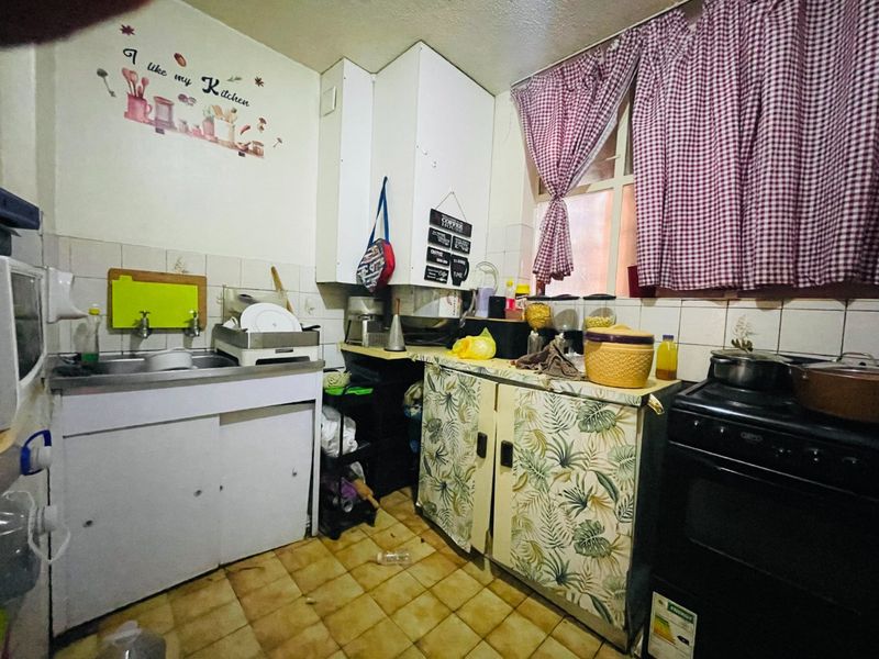 A compact kitchen featuring a stainless steel sink, tiled backsplash, and dated cabinetry, offering significant potential for a modern renovation and layout update.