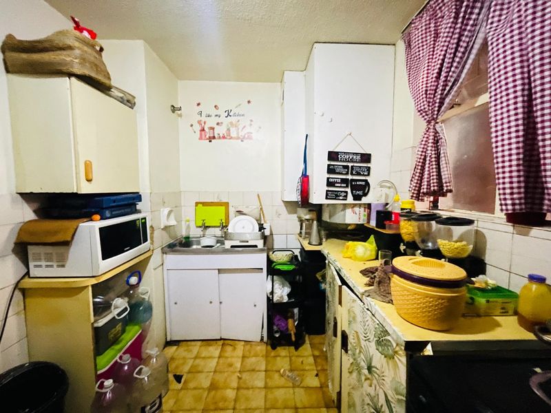 A compact kitchen featuring built-in cabinetry, a stainless steel sink, and tiled finishes, currently showing significant signs of wear and dated fixtures.