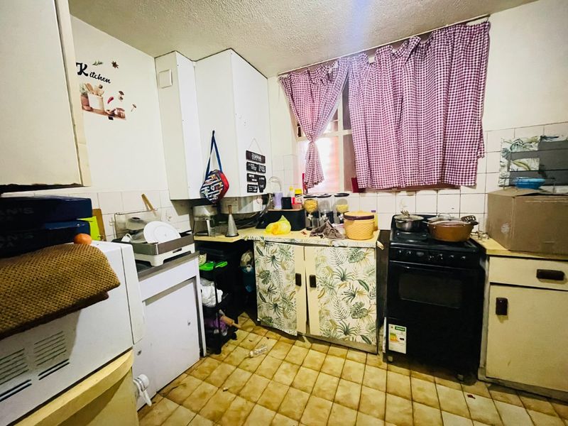 A dated kitchen featuring original cabinetry, tiled flooring, and a freestanding stove, offering significant potential for modernization and renovation.