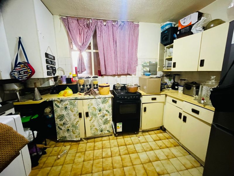 A dated kitchen featuring original cabinetry, a freestanding stove, and tiled flooring, offering significant potential for modernization and renovation.