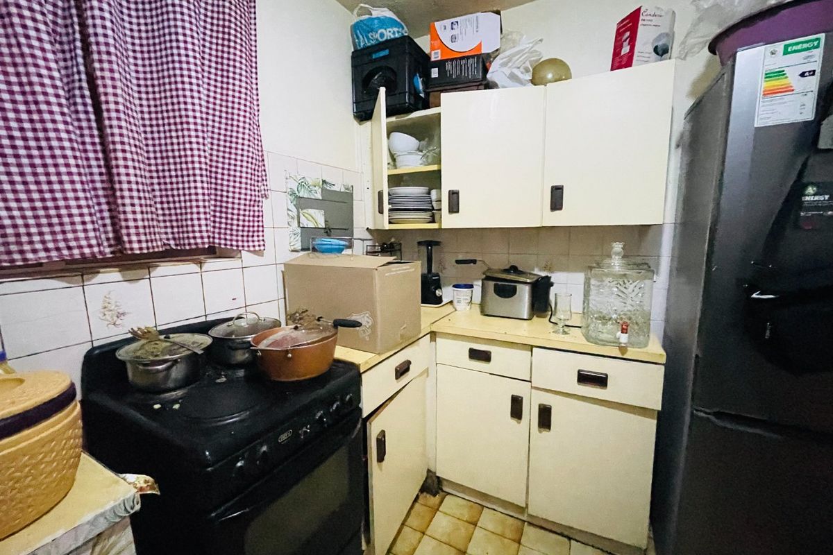 A compact kitchen featuring dated cabinetry, tiled backsplash, and floor tiles, requiring modernization to improve functionality and aesthetic appeal.