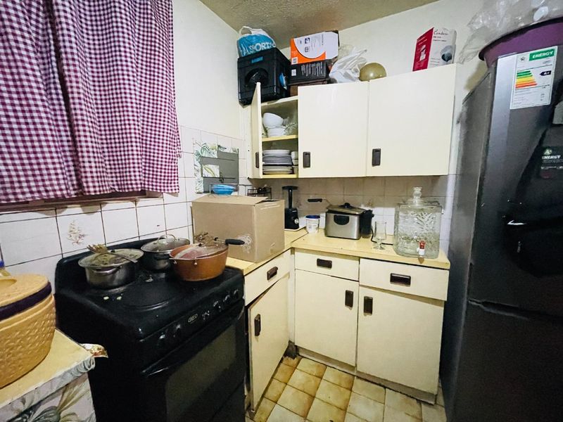 A compact kitchen featuring dated cabinetry, tiled backsplash, and floor tiles, requiring modernization to improve functionality and aesthetic appeal.