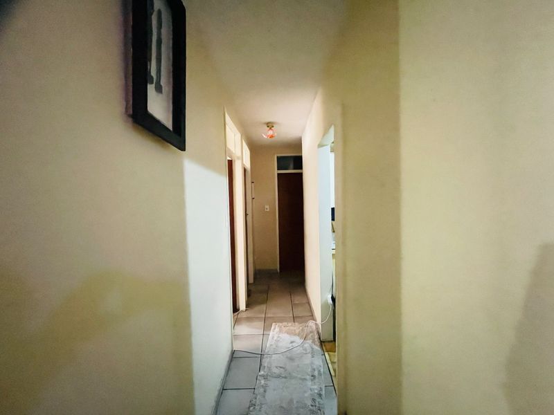 A narrow residential hallway featuring tiled flooring and multiple internal access points, requiring cosmetic updates to improve the overall aesthetic.
