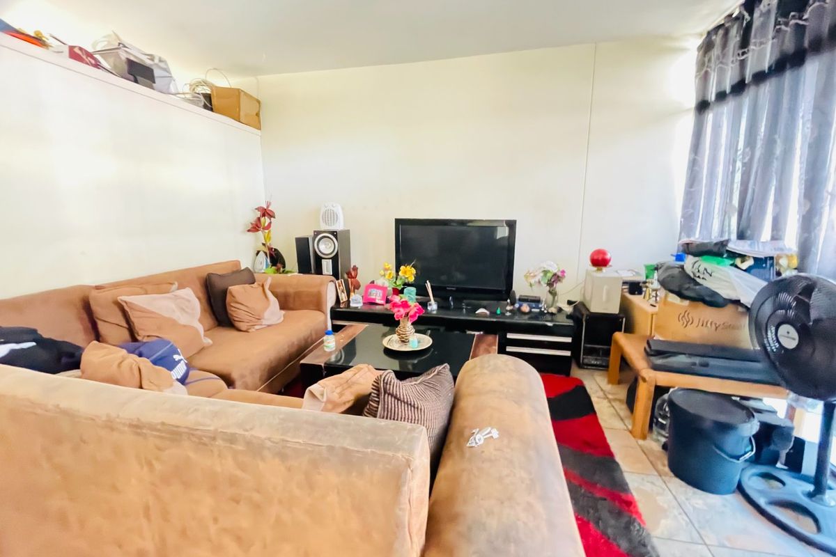 A living room area featuring tiled flooring and large windows with curtain rails, offering a functional space for relaxation.