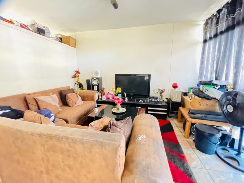 A living room area featuring tiled flooring and large windows with curtain rails, offering a functional space for relaxation.