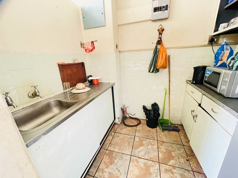 A compact scullery area featuring a stainless steel sink, tiled splashbacks, and built-in cabinetry, requiring cosmetic updates to improve its overall condition.