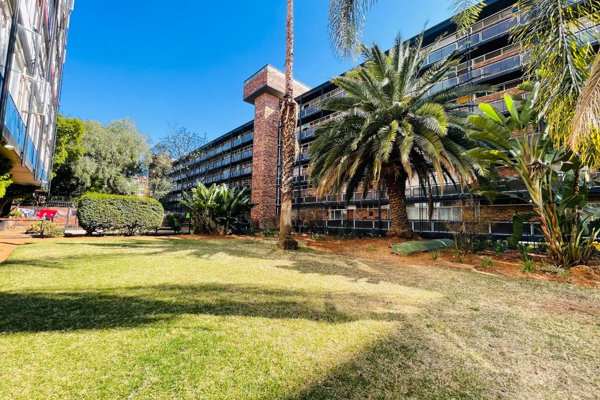 A view of the apartment building exterior featuring a brick facade, multiple balconies, and a well-maintained communal garden area.