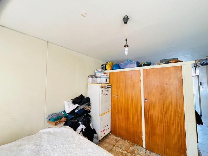 A bedroom featuring built-in wooden cupboards and tiled flooring, currently showing signs of wear and requiring cosmetic updates.