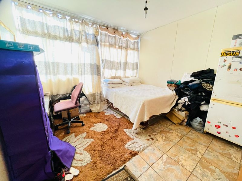 A bedroom featuring tiled flooring and a large window, providing natural light. The space requires cosmetic updates to improve its overall condition.