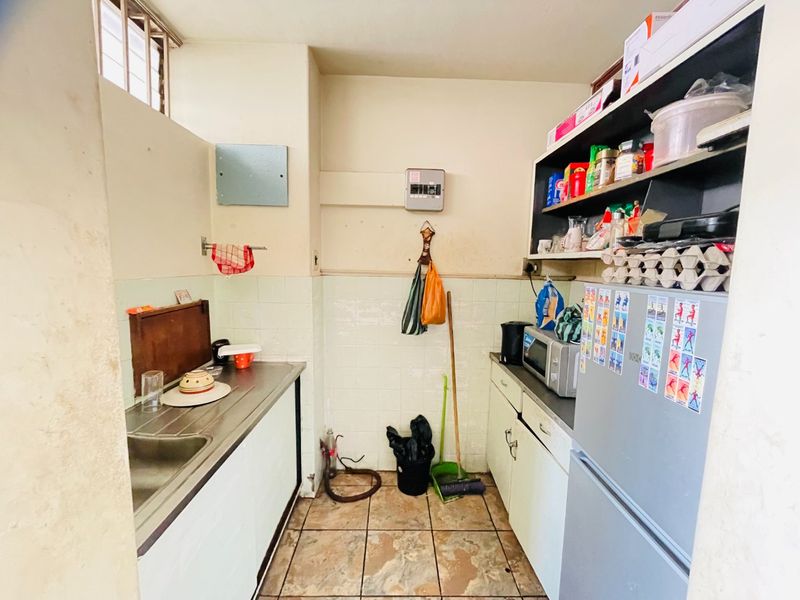 A functional scullery area featuring a stainless steel sink, tiled splashback, built-in cabinetry, and tiled flooring, providing practical utility space.