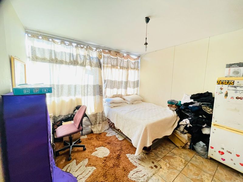 A bedroom featuring tiled flooring and a large window, providing natural light. The space is ready for a refresh to enhance its appeal.