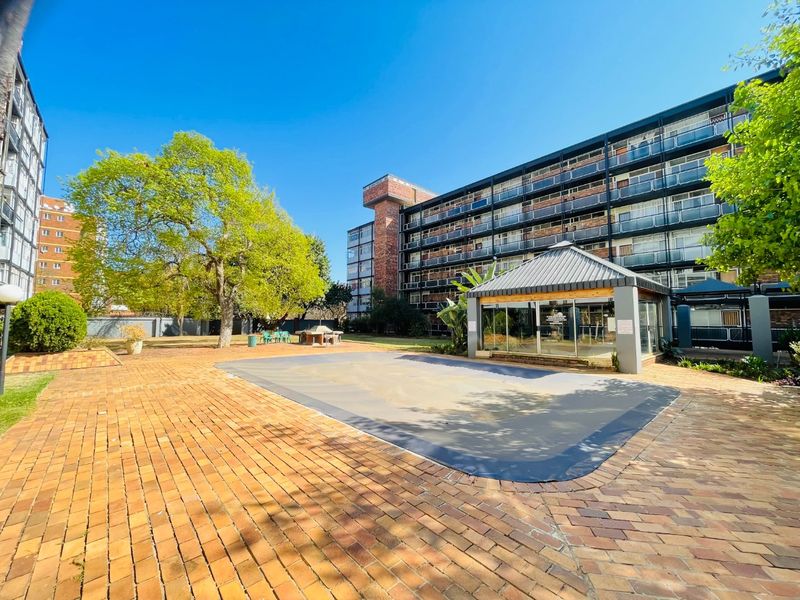 Communal outdoor area featuring a swimming pool with a cover, brick paved surrounds, and a gazebo, set within an apartment complex.