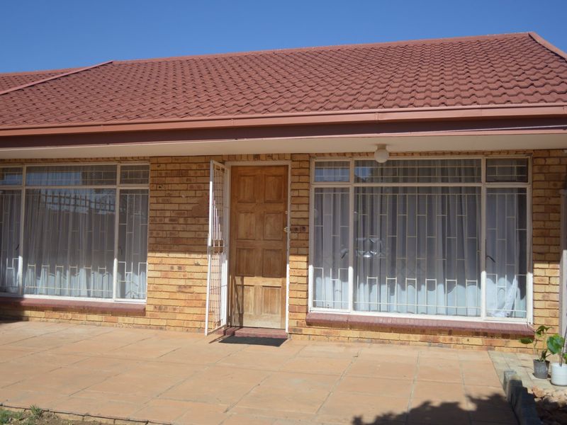 Front elevation of a face brick townhouse featuring a tiled roof, paved patio area, and secure window treatments.