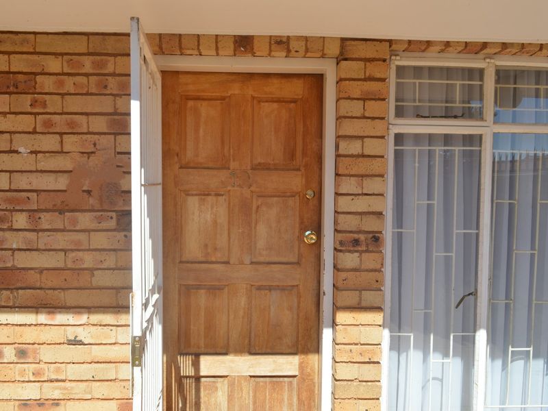Exterior view of the townhouse entrance featuring a timber panel door, security gate, and face brick facade.