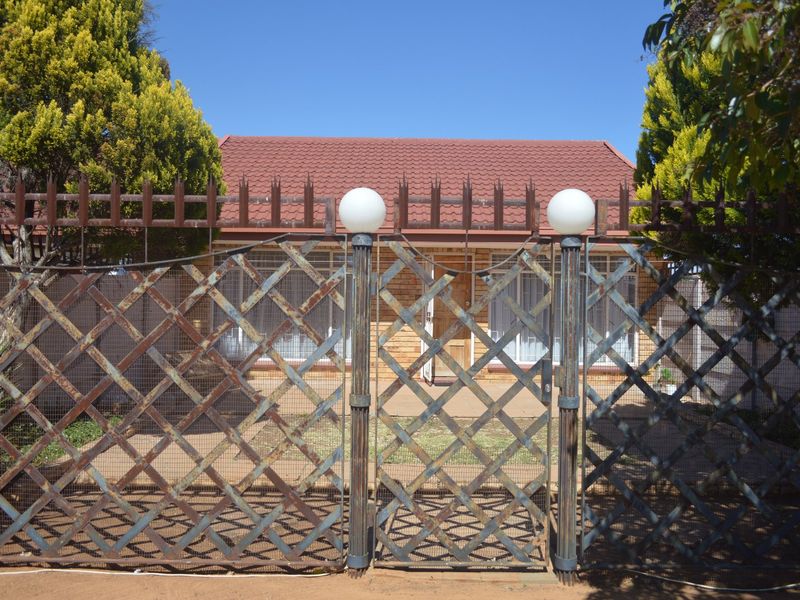 Front view of a townhouse featuring a brick facade, tiled roof, and a metal security gate with perimeter fencing.