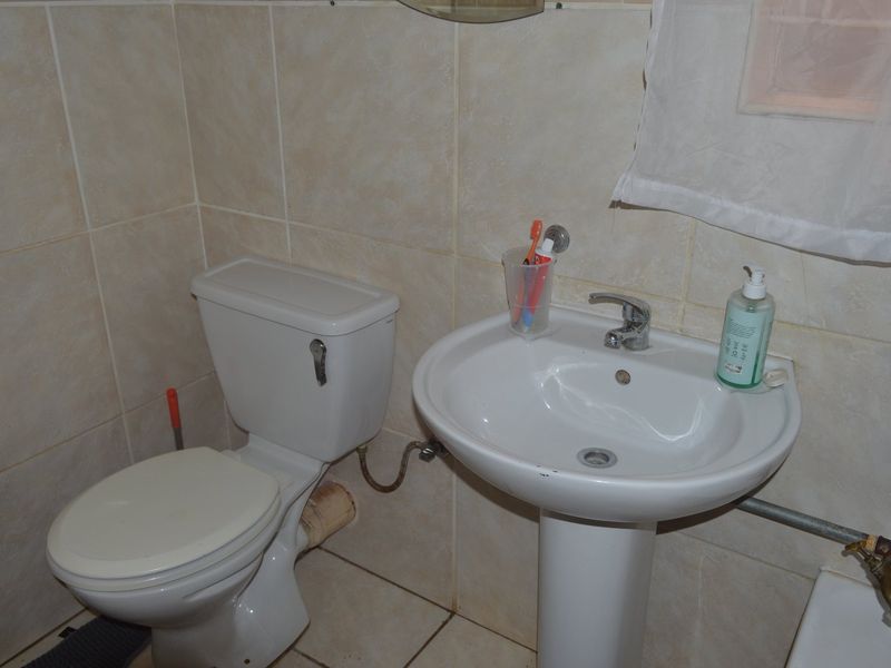 A compact bathroom featuring a pedestal washbasin and ceramic toilet with tiled wall and floor finishes.