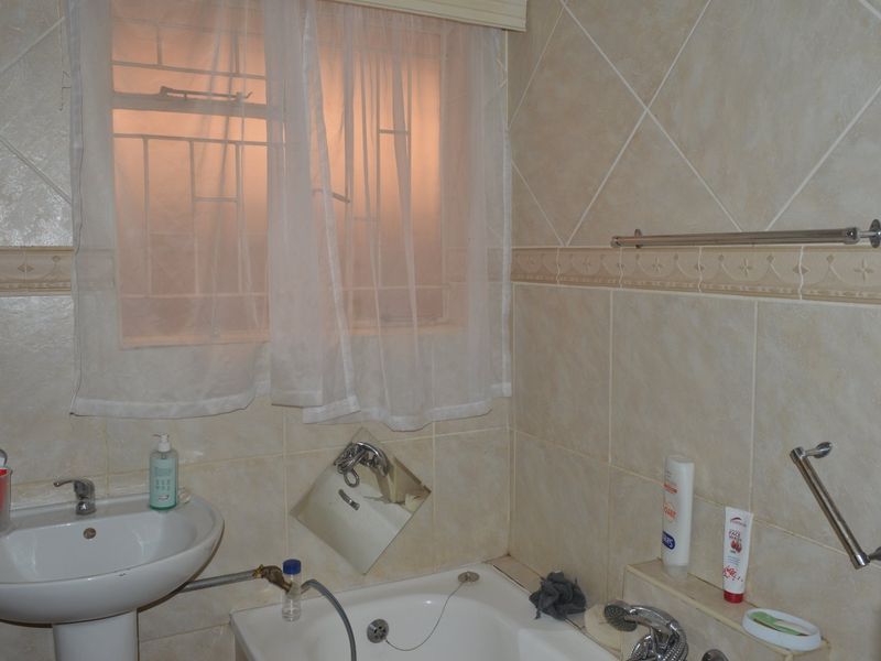A functional bathroom featuring a pedestal basin, built-in bathtub with chrome fixtures, and neutral wall tiling with a decorative border.