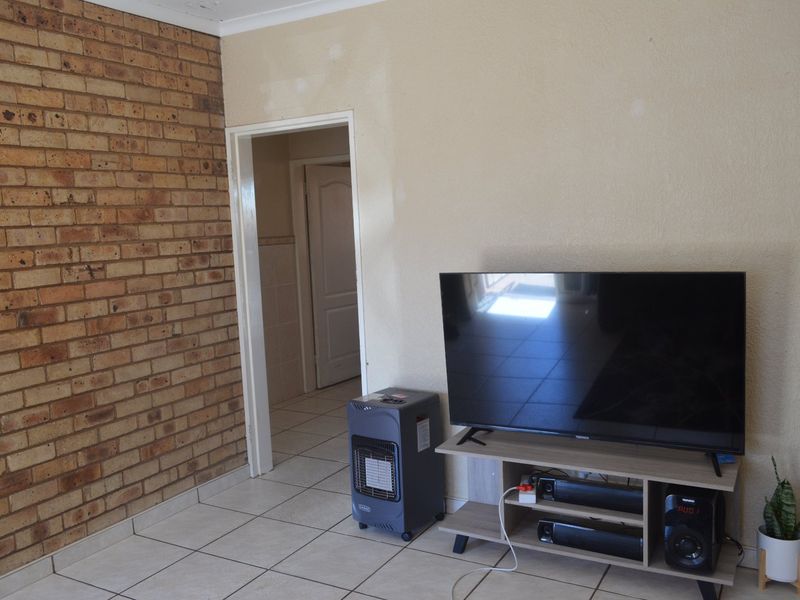 Living room featuring an exposed brick accent wall, ceramic floor tiles, and coved ceiling cornice, requiring minor cosmetic wall repairs.