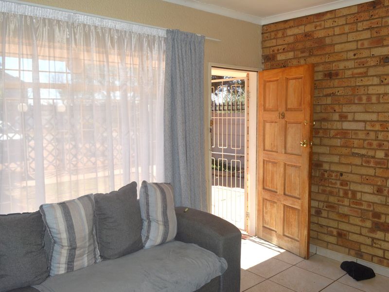 Living room featuring an exposed brick feature wall, tiled flooring, and direct access to the exterior through a timber door with a security gate.