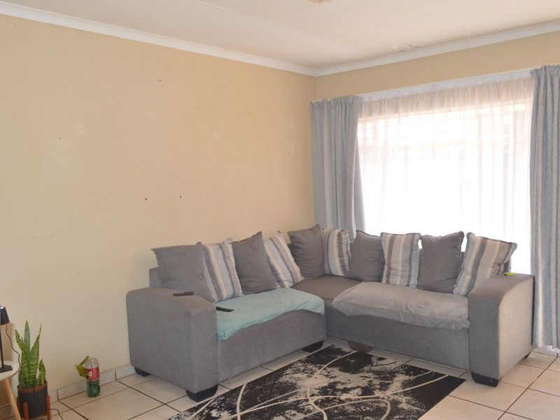A living room featuring tiled flooring and coved ceilings, currently showing signs of wear including ceiling damage.