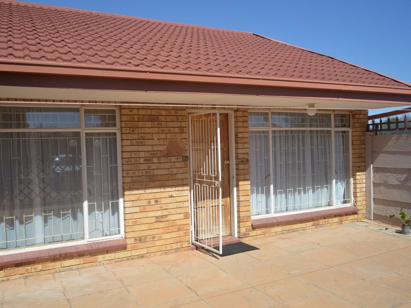 Rear exterior view of the townhouse featuring a paved patio, brick facade, tiled roof, and secure entrance with security gate and window bars.