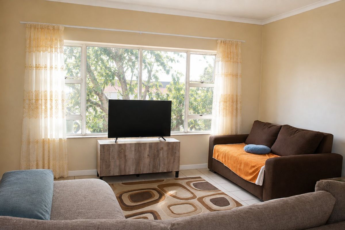 A bright living room featuring large windows that provide natural light and a view of the surrounding greenery.