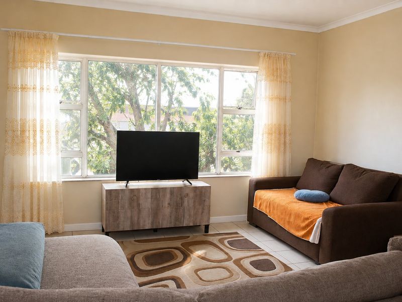 A bright living room featuring large windows that provide natural light and a view of the surrounding greenery.