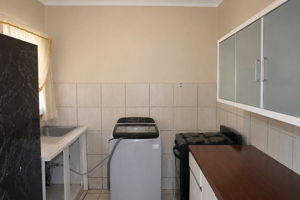 Functional kitchen area featuring a stainless steel sink, tiled splashback, electric stove, and wall-mounted cabinetry with some open storage space.