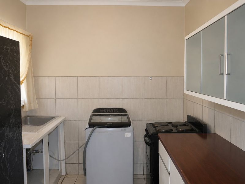 Functional kitchen area featuring a stainless steel sink, tiled splashback, electric stove, and wall-mounted cabinetry with some open storage space.