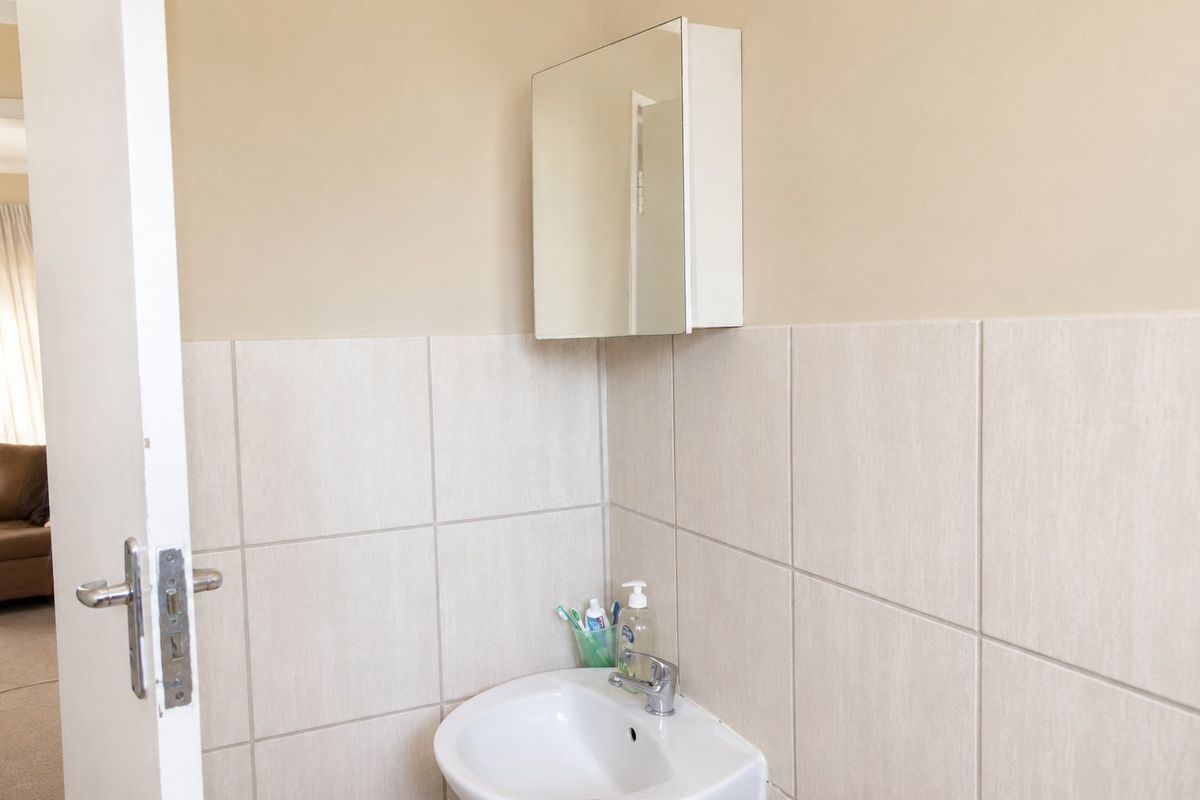 A functional bathroom featuring a wall-mounted mirror cabinet, a ceramic basin with a chrome mixer tap, and neutral wall tiling.