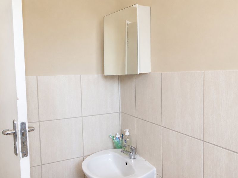 A functional bathroom featuring a wall-mounted mirror cabinet, a ceramic basin with a chrome mixer tap, and neutral wall tiling.