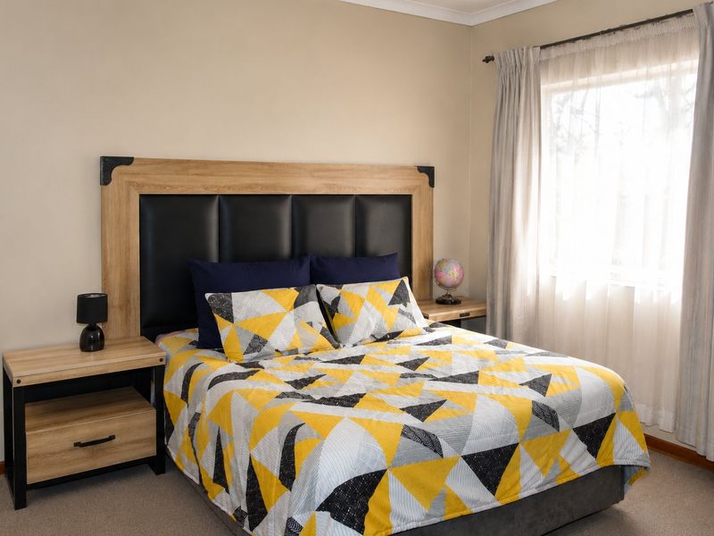 A well-maintained bedroom featuring neutral wall tones, carpeted flooring, and a window fitted with a curtain rod.